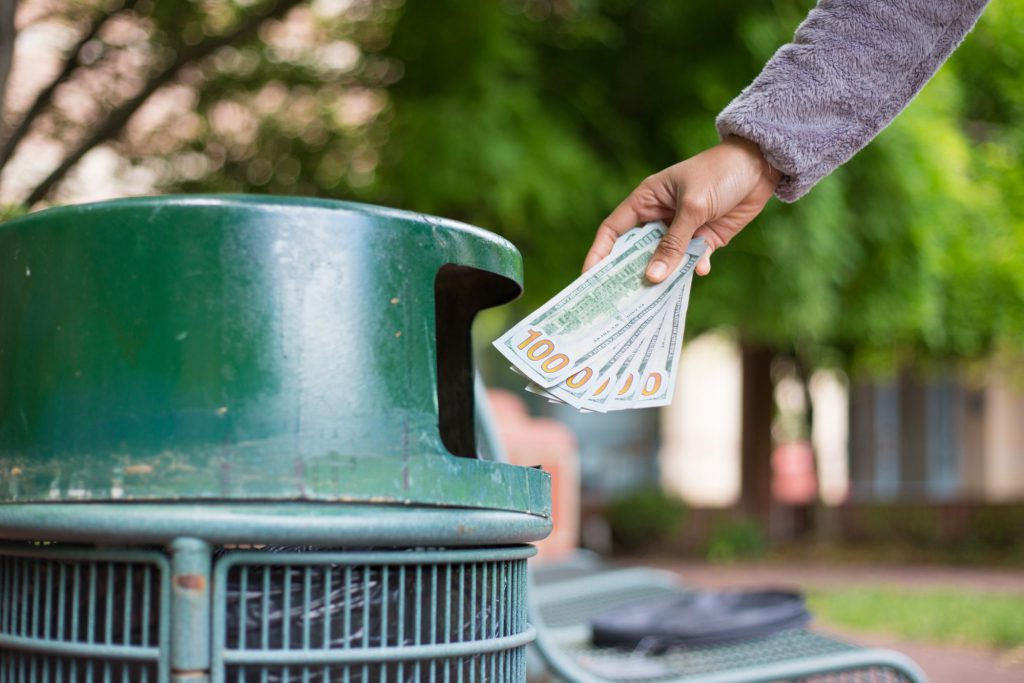 Hand throwing money in trash